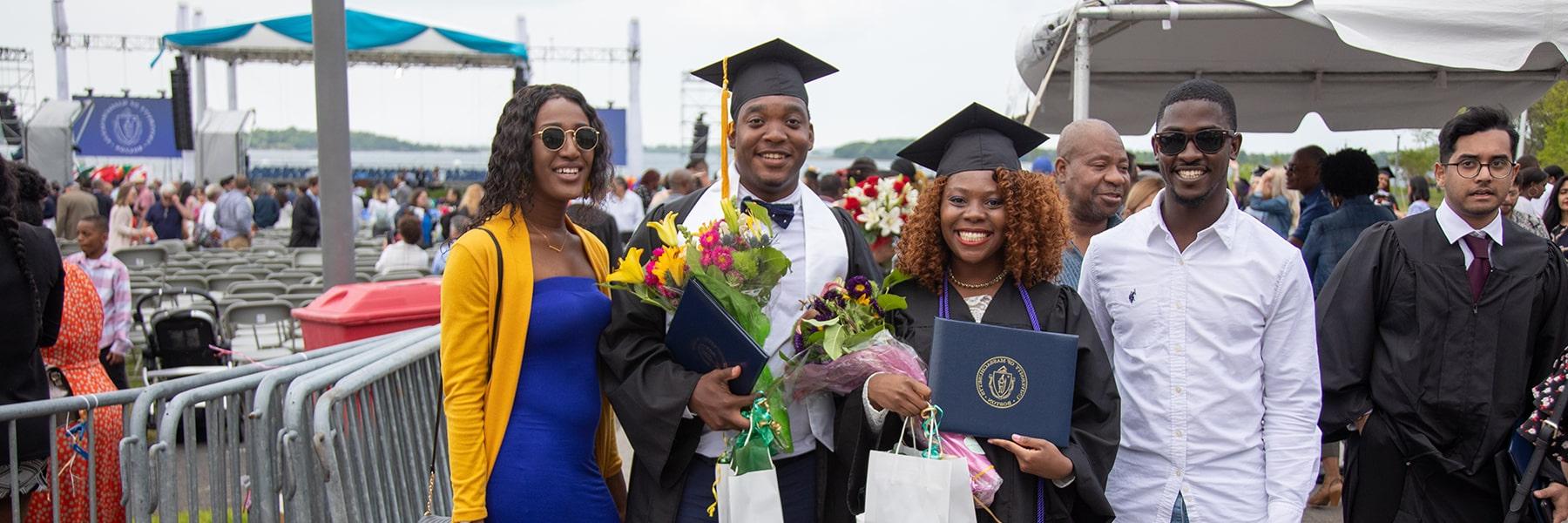 Students hold flowers standing with friends & families at Commencement.